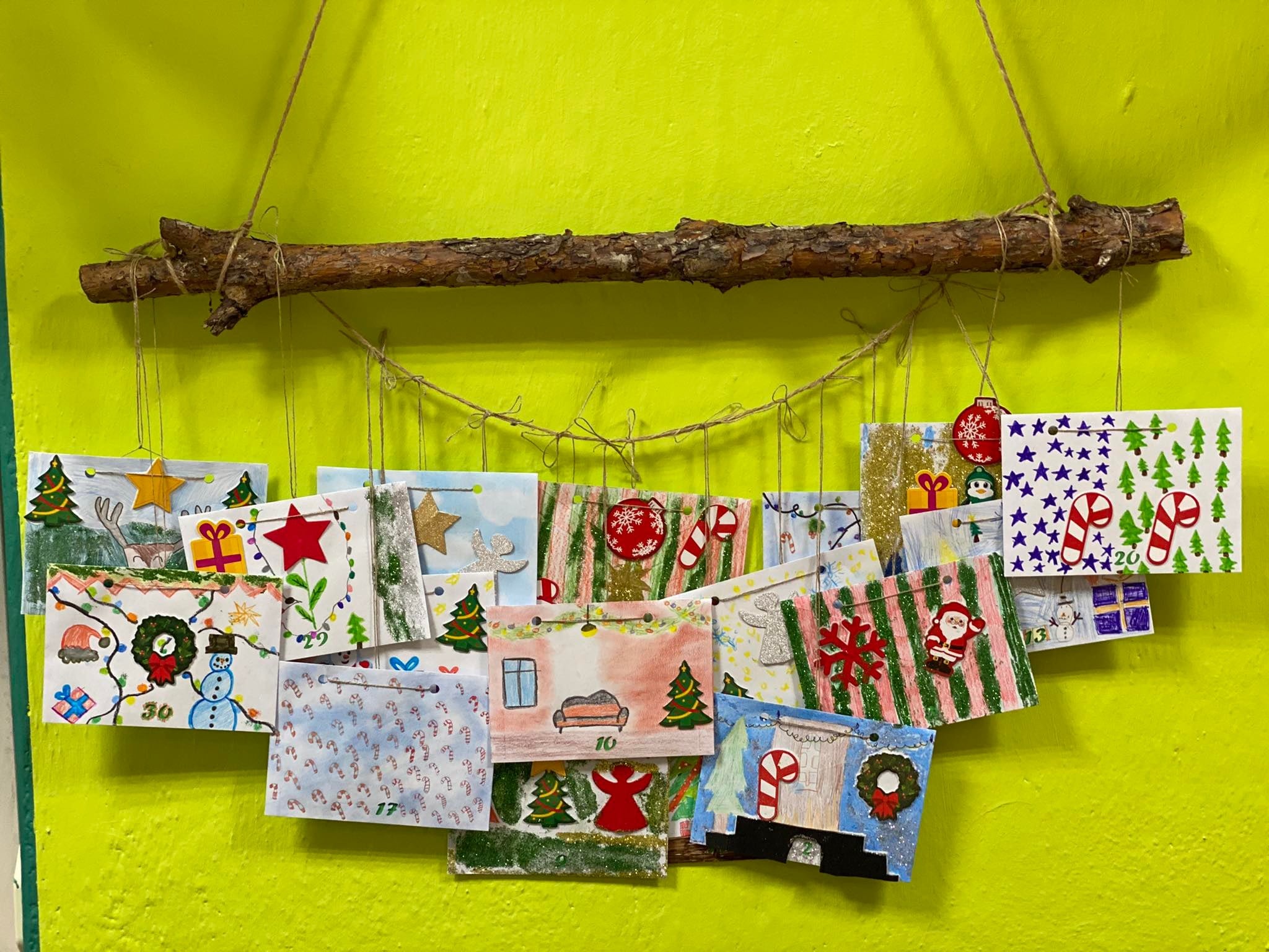 Kolorowe świąteczne kartki przyczepione na sznurku do gałęzi i przyczepione do ściany